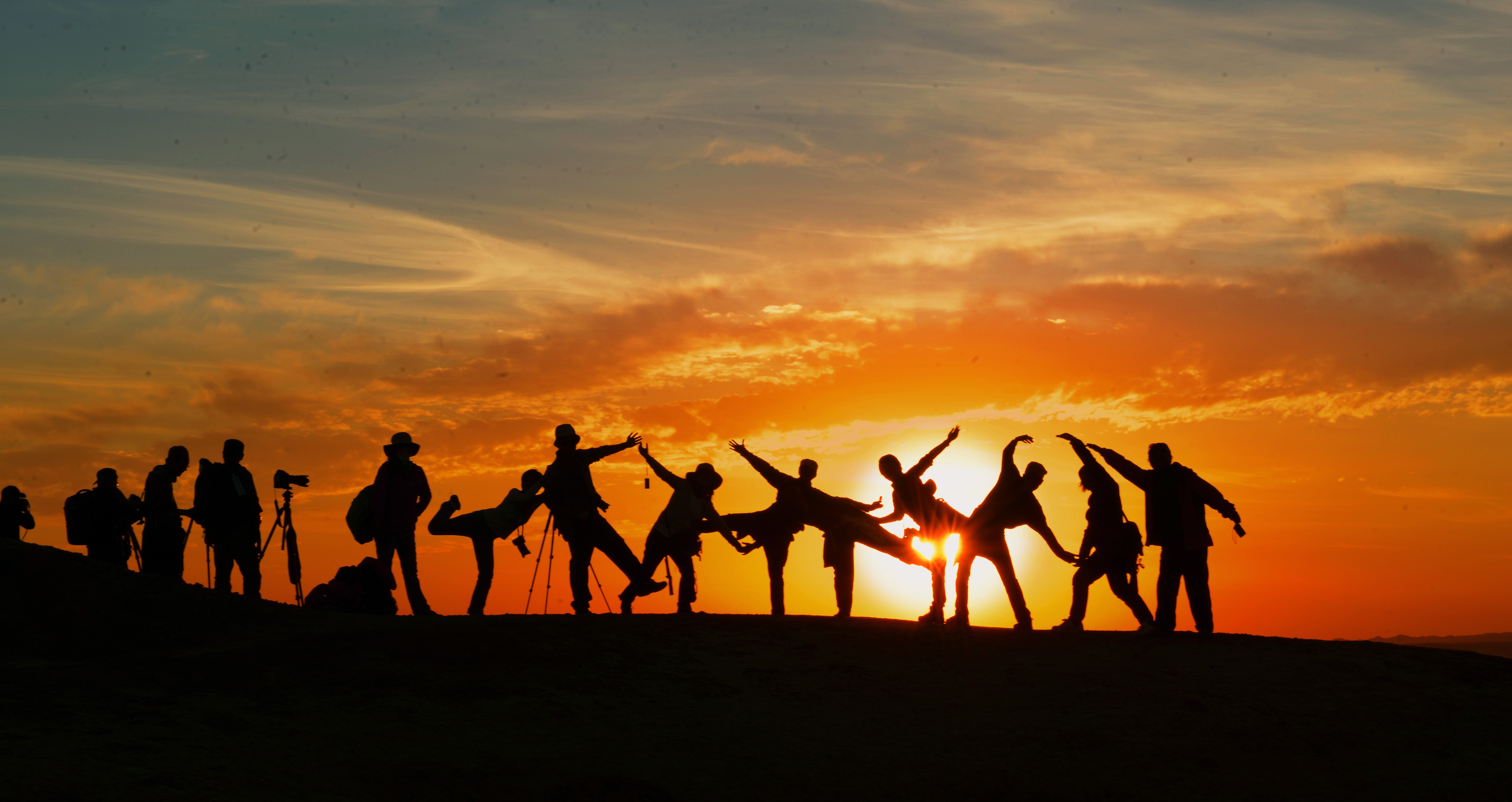 silhouetted people on a hilltop with sun setting behind them